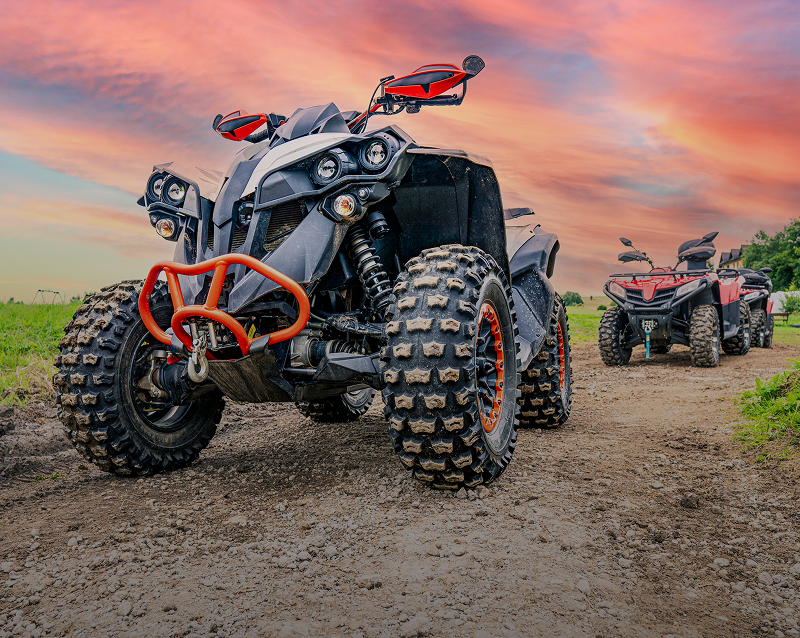 Two ATVs on a dirt path, sunset.