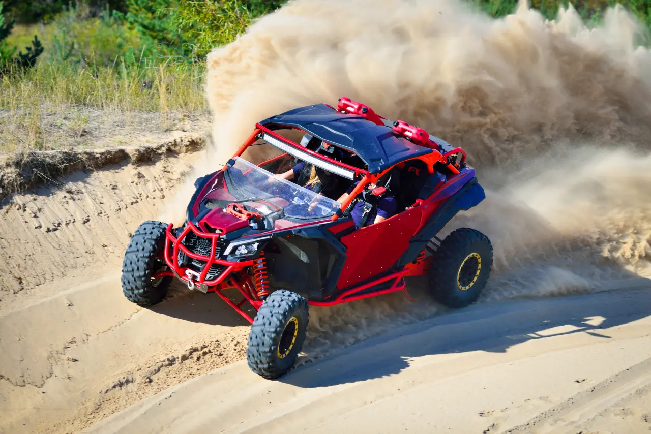 Red off-road vehicle racing on sandy terrain.