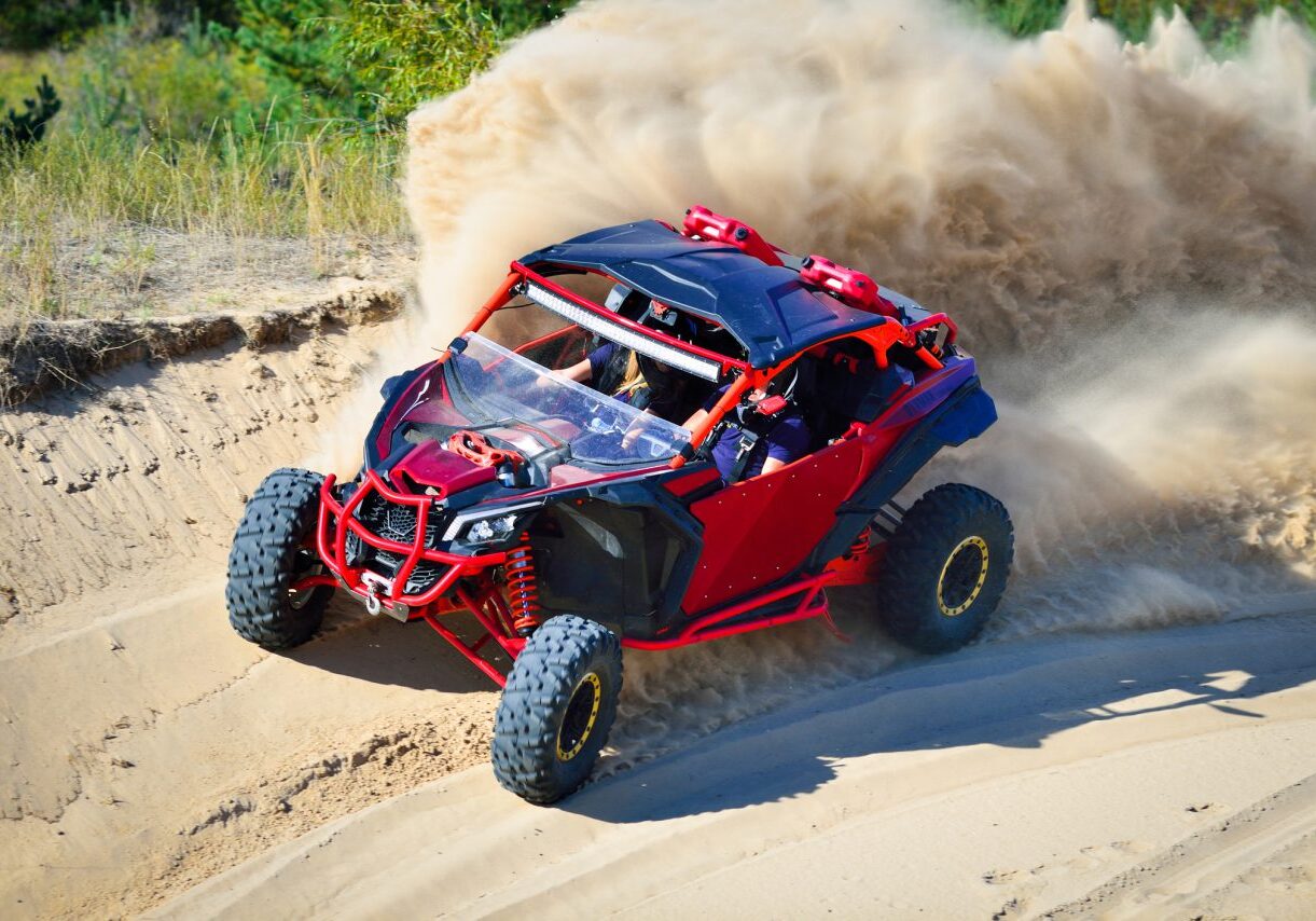 Red off-road vehicle racing on sandy terrain.